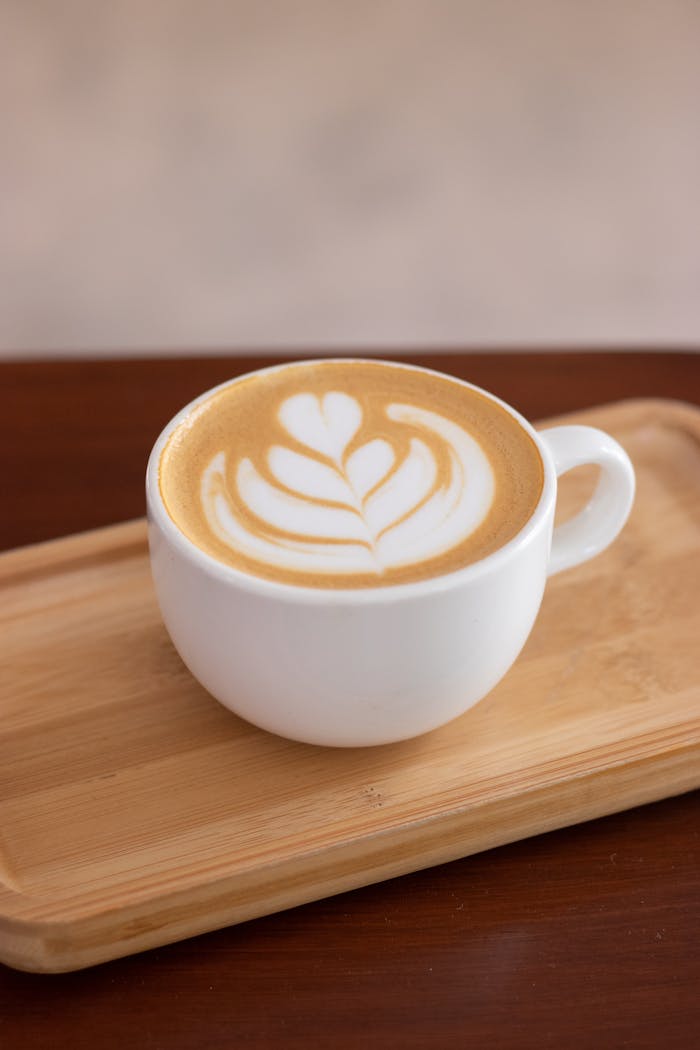 Beautiful latte art in a white cup on a wooden tray, capturing coffee culture.