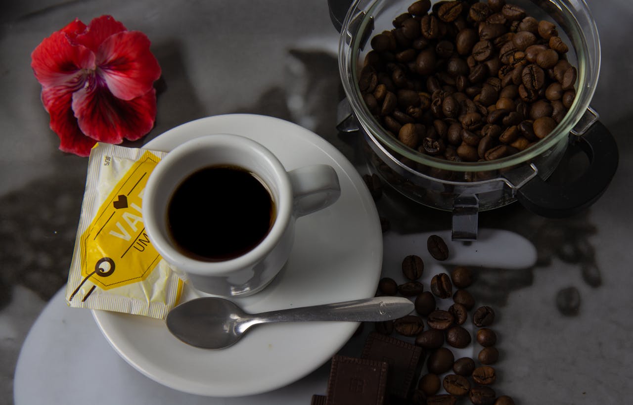 Aesthetic overhead view of coffee setup with beans, cup, and vibrant red flower.